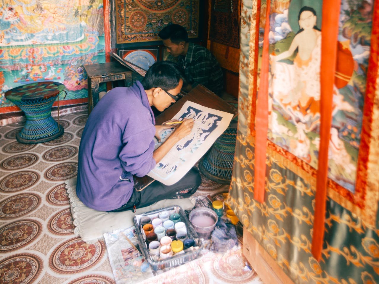 Artisan carefully painting a Buddhist thangka in an indoor workshop, showcasing intricate artistry and cultural heritage.